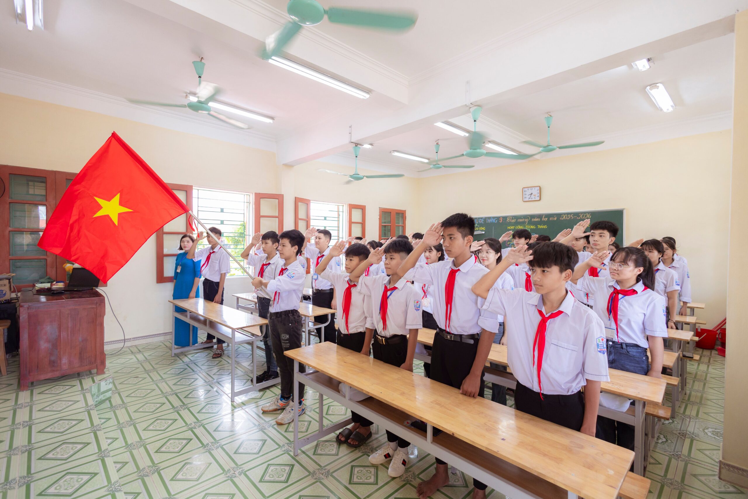 Students saluting the Vietnamese flag inside a bright classroom, demonstrating national pride and unity.